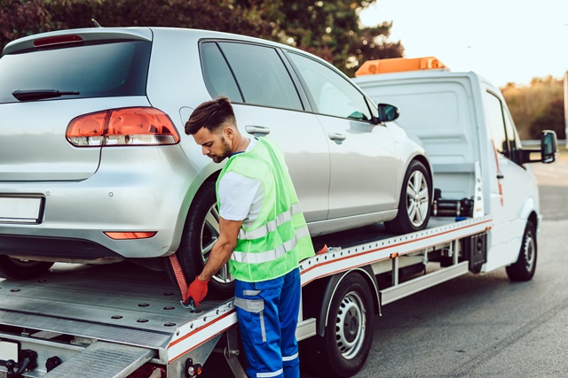 Fahrer vom Abschleppdienst sichert Pannenfahrzeug