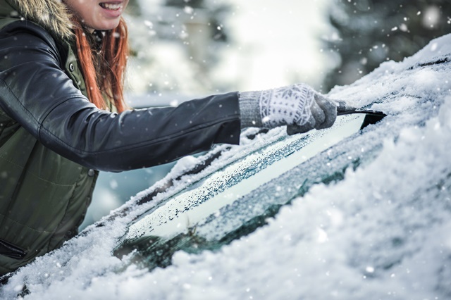 Frau befreit Windschutzscheibe von Schnee und Eis