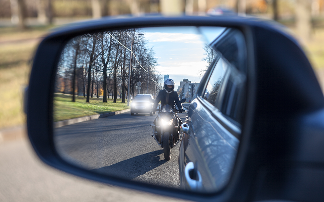 Auto-Seitespiegl darin zusehen: Motorradfahrer mit Tagfahrlicht