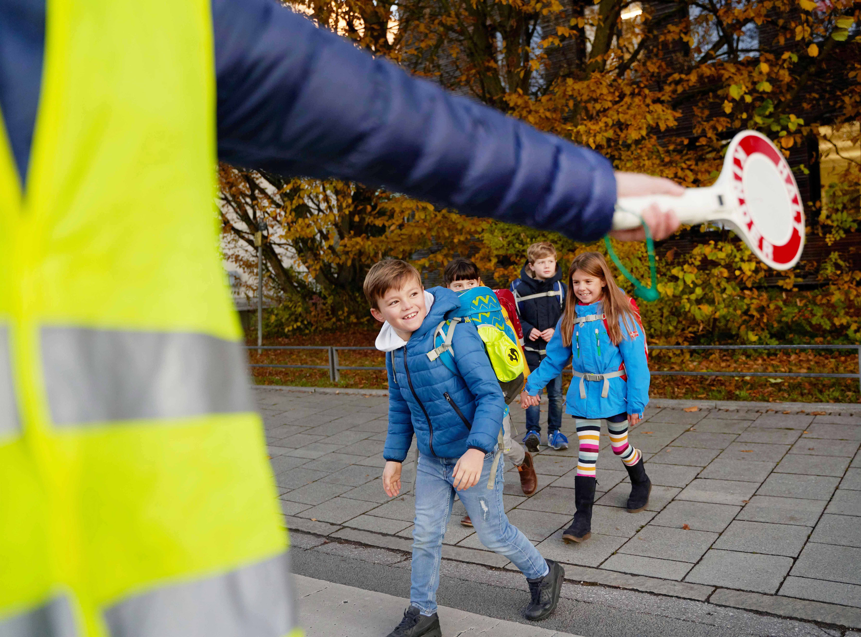 Schulkinder überqueren Straße, Schullotse sperrt mit Kelle ab