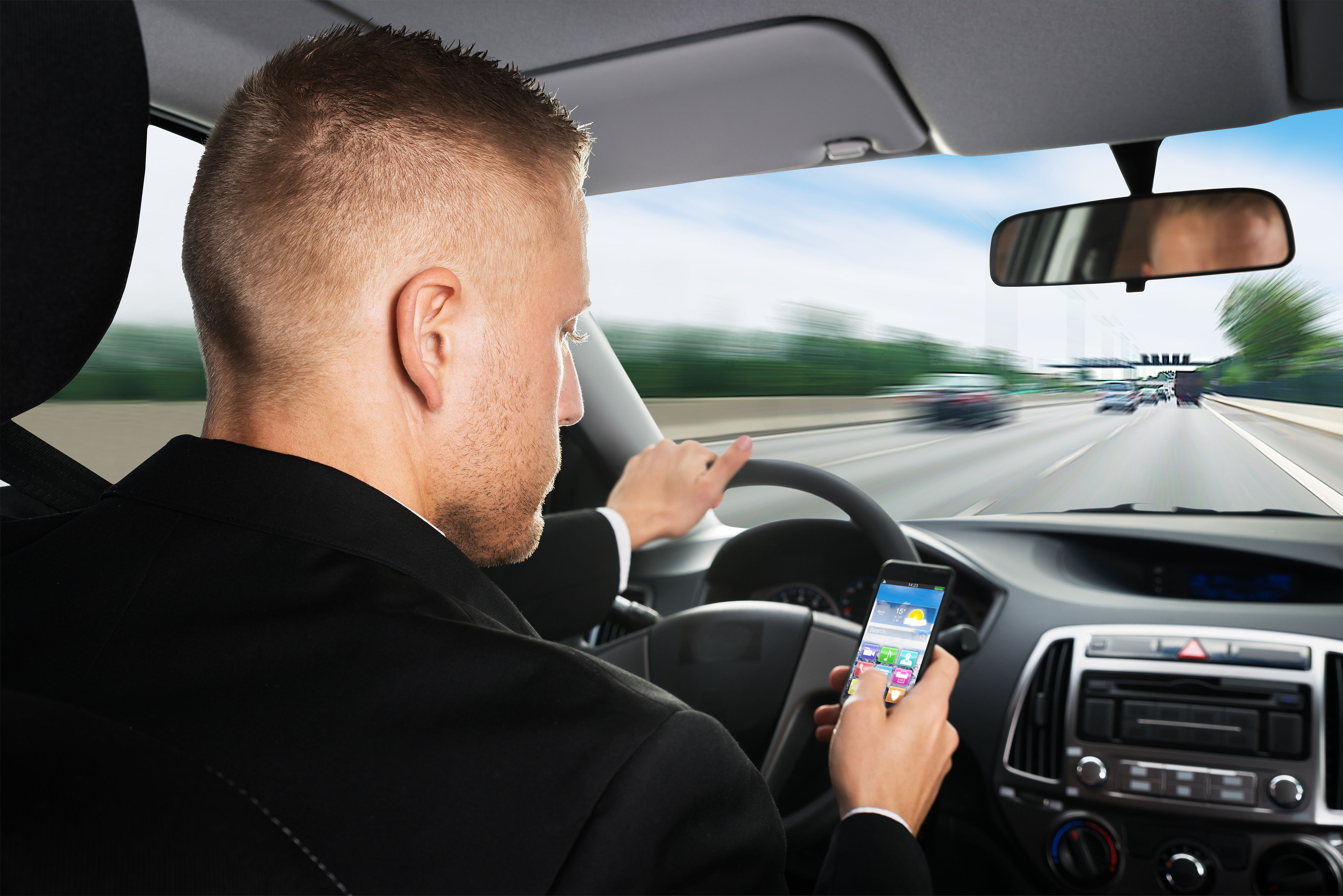 Fahrer schaut auf Smartphone während der Fahrt